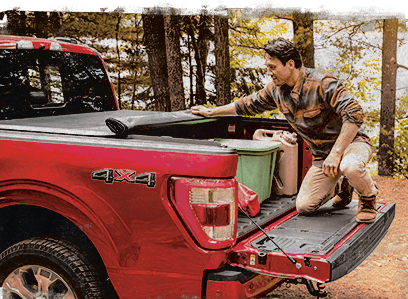 Man in the woods rolling up a WeatherTech Roll Up Pickup Truck Cover.