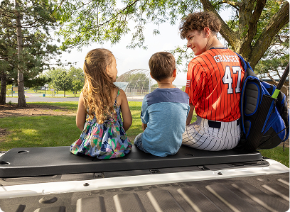 three children sitting on tailgate cushion after sporting event