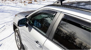 Image of white S U V with side window deflectors installed driving in the snow