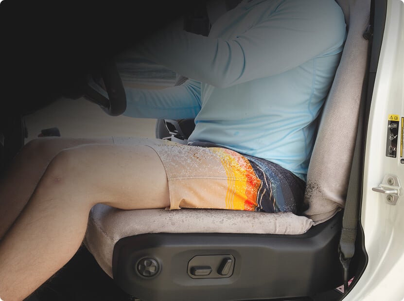 man in swim suit covered in sand sitting on terry cloth seat cover