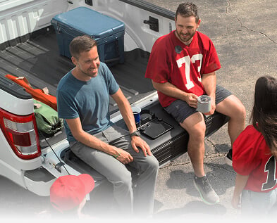 Sports fans sitting on a truck tailgate with WeatherTech Tailgate Cushion installed.