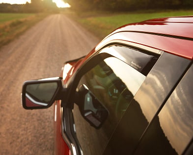 WeatherTech Side Window Deflector installed on a vehicle driving down a country road.