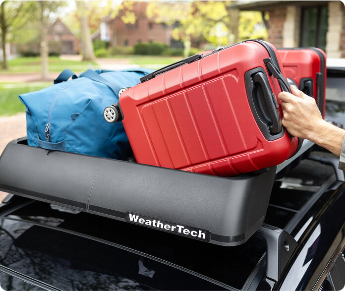 Person loading luggage into a WeatherTech Roof Basket.